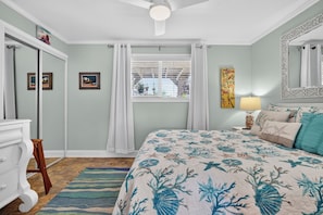 A bedroom with a bed, a dresser, a window with curtains, a painting, and a lamp. - Pet Friendly Apartment- Walk To The Beach (Palm Coast)