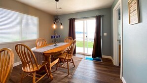 A dining area with a wooden table and chairs, a chandelier, and a view through a glass door to the outdoors.