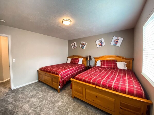 Un dormitorio con dos camas de madera, cada una con ropa de cama a cuadros rojos, una lámpara de techo y una puerta a la izquierda.