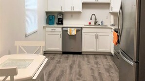 A compact kitchen with white cabinets, a stainless steel refrigerator, a coffee maker, and a dishwasher. - Beach Cottage, Steps to Beach. Updated and Great Deal for Money. Pet Friendly. (Fort Pierce)