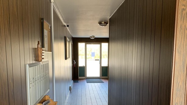 Un couloir aux murs recouverts de lambris en bois, doté d’un sol carrelé et d’une porte donnant sur l’extérieur.