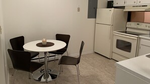 Une cuisine compacte avec un réfrigérateur blanc, une cuisinière et un four à micro-ondes. On y trouve une petite table à manger avec quatre chaises.