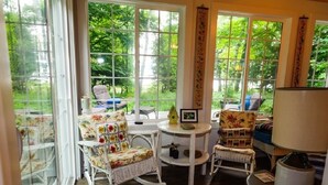 A cozy room with large windows, wicker furniture, and a small table with a lamp. - Year round Crystal Lake cottage, newly remodelled 4br/1ba, w/sandy beach! (Frankfort)