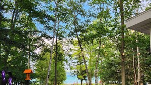 An outdoor deck with seating, surrounded by trees and a view of the water. - Year round Crystal Lake cottage, newly remodelled 4br/1ba, w/sandy beach! (Frankfort)