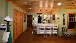 A cozy kitchen with wooden ceiling beams, a dining area with white chairs, and a staircase leading to another level. - Year round Crystal Lake cottage, newly remodelled 4br/1ba, w/sandy beach! (Frankfort)