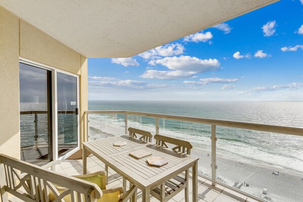 A balcony with a view of the ocean, a wooden table, and a chair.