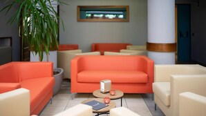 A lobby with orange sofas, beige armchairs, and a small table with a book and a candle. - Hotel Giardino (Cannobio)