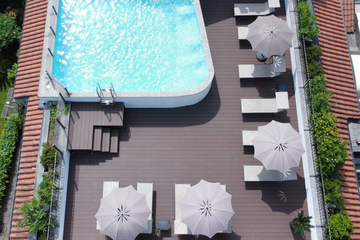 Vista aérea de una piscina en la azotea con terraza de madera, sillas de descanso y sombrillas.