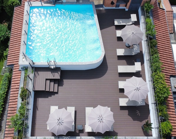 Vista aérea de una piscina en la azotea con terraza de madera, sillas de descanso y sombrillas.