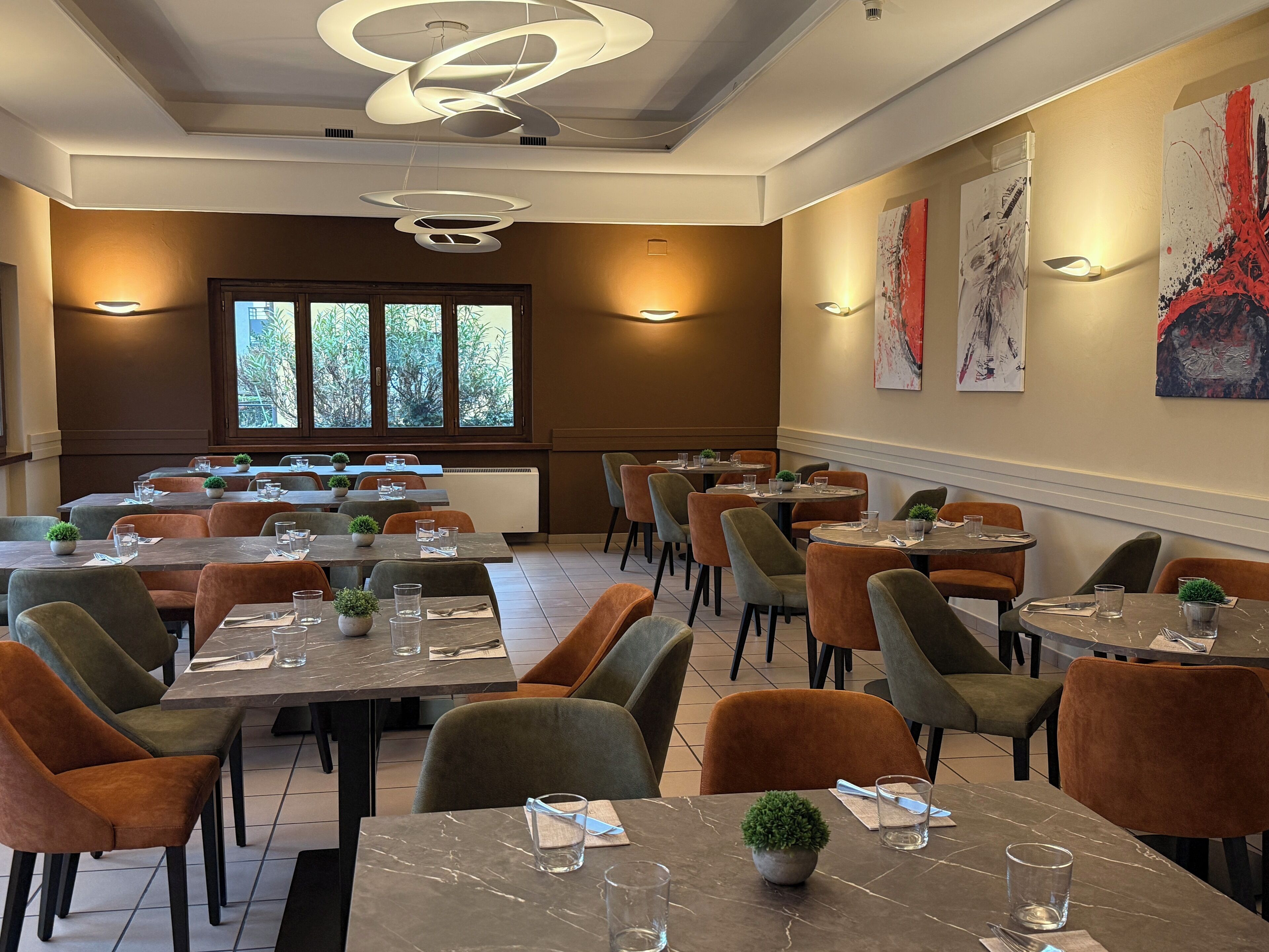 A restaurant with multiple tables and chairs, large windows, and modern lighting fixtures.
