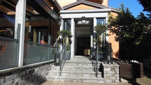 A building with a stone facade, a set of steps leading to a door, and a small garden area with potted plants. - Hotel Giardino (Cannobio)