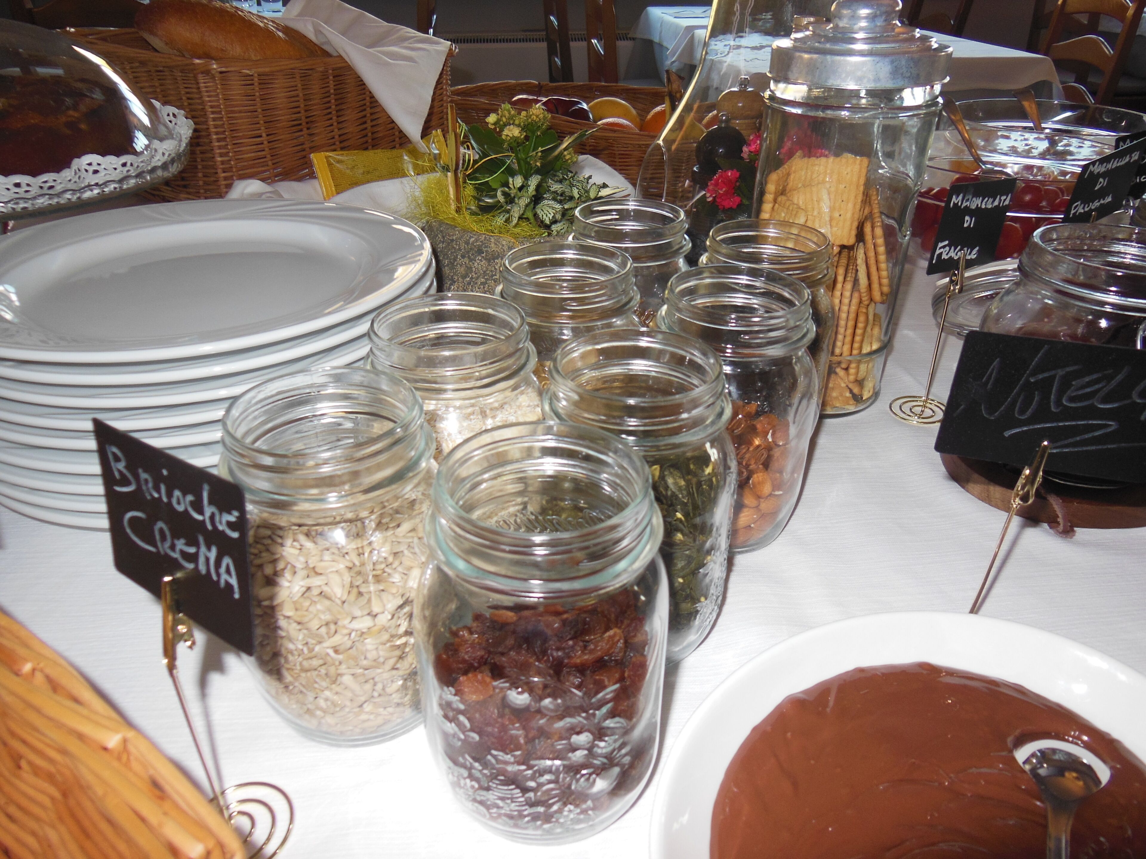 A buffet table with various food items and condiments, including jars of pickles, nuts, and a chocolate dessert.