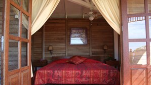 Una habitación de madera con una cama, cortinas, ventilador de techo y ventana.