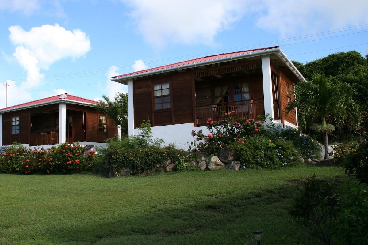 A two-story wooden house with a red roof, white walls, and a balcony.