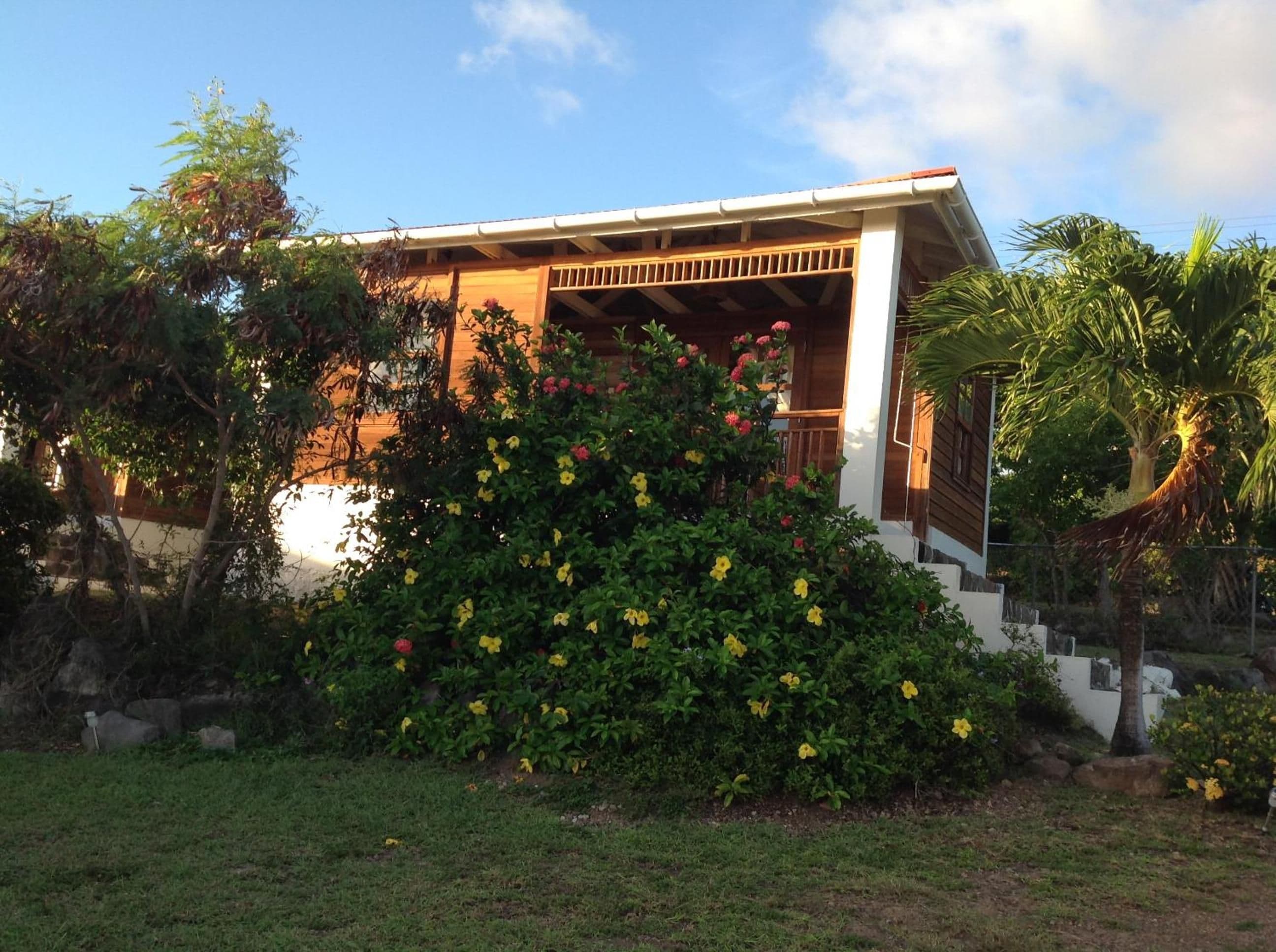A house with a covered porch, surrounded by lush greenery and flowering plants.