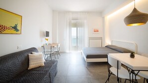A modern, well-lit room with a bed, a sofa, a dining table, and a hanging light fixture. - Salsedine Sea View (Salerno)