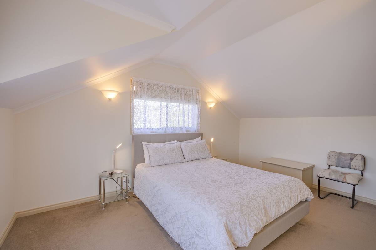 A bedroom with a bed, a nightstand, a chair, and a window with a lace curtain.
