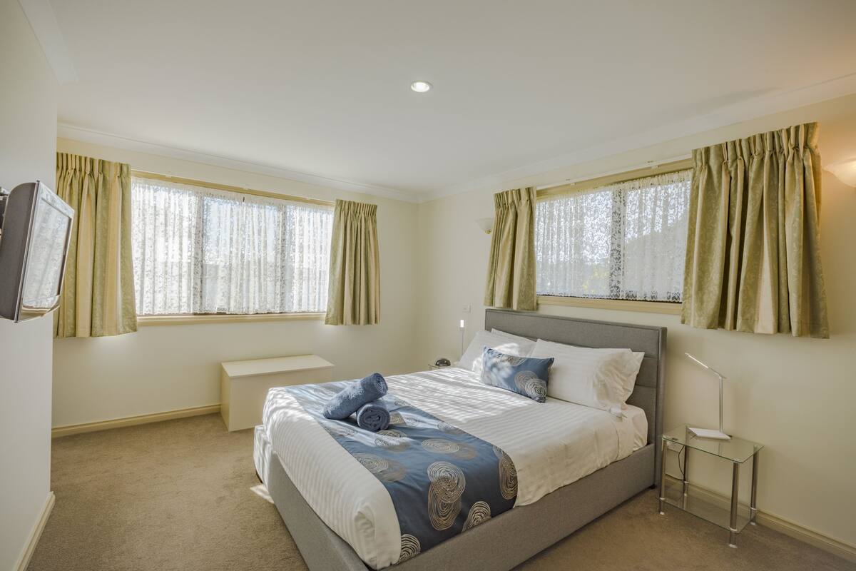A bedroom with a bed, bedside tables, a TV, and curtains.