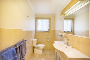 Un baño con inodoro, lavamanos y una ventana con cortina.