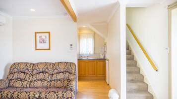 A living room with a patterned sofa, a kitchen with wooden cabinets, and a carpeted staircase.