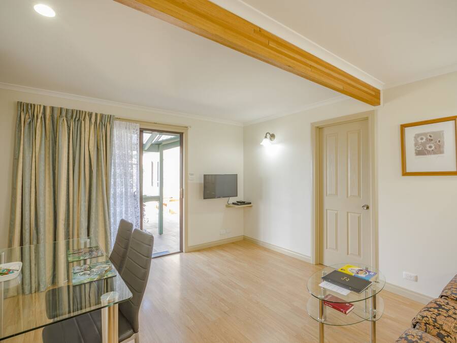 A living room with a glass table, a sofa, a television, and a door leading to another room.