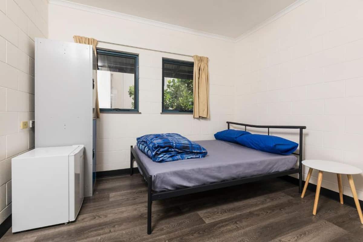 A small, compact room with a bed, a small white appliance, and a window with curtains.