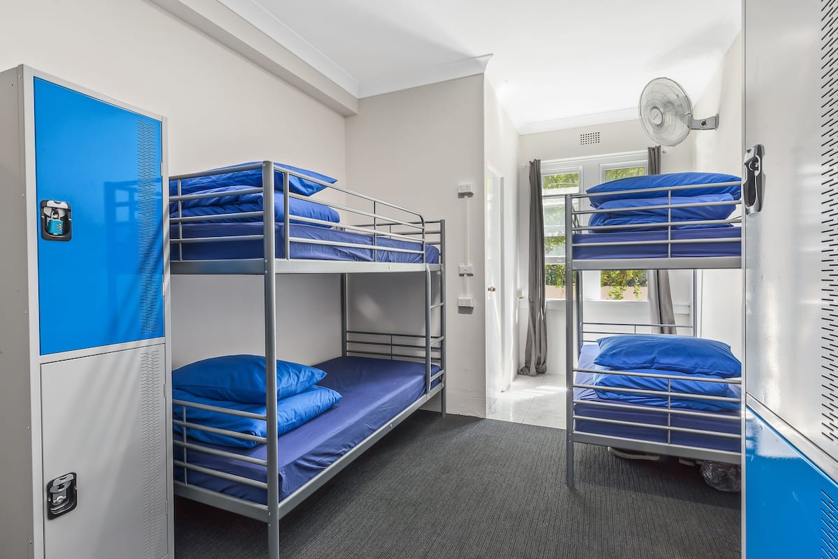 A dormitory room with bunk beds, a wardrobe, and a fan.