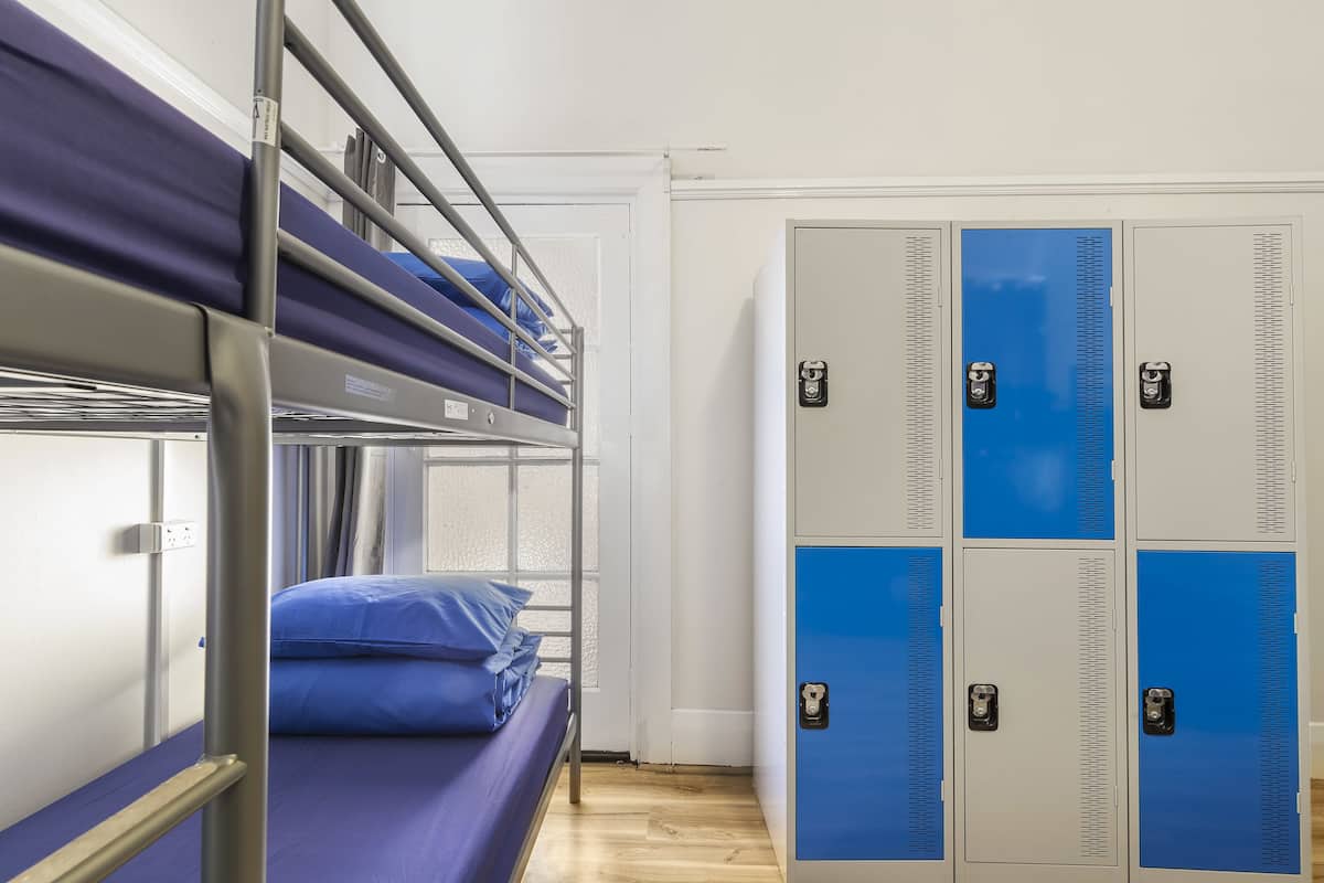 A bunk bed with blue bedding, a metal ladder, and a wooden floor.