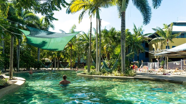 A pool area with clear water, surrounded by palm trees and a shaded area. - Summer House Backpackers Cairns (Cairns North)