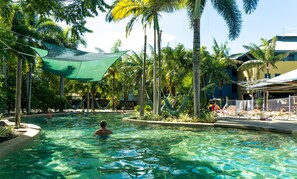 A pool area with clear water, surrounded by palm trees and a shaded area. - Summer House Backpackers Cairns (Cairns North)