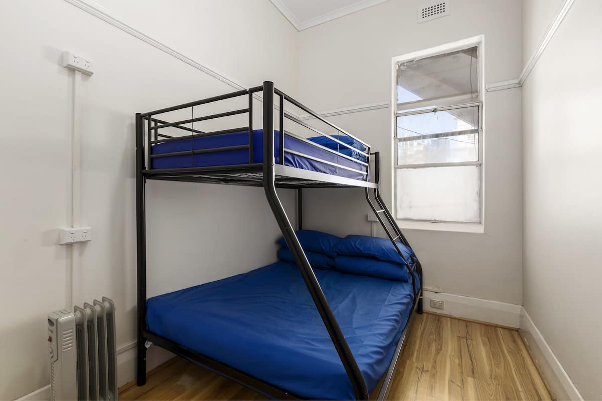 A bunk bed with blue bedding in a room with white walls and a window.