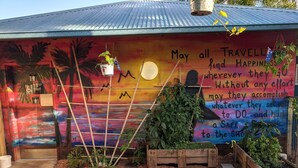 A colorful mural with motivational text, a toilet sign, and a wooden planter with plants. - Summer House Backpackers Cairns (Cairns North)