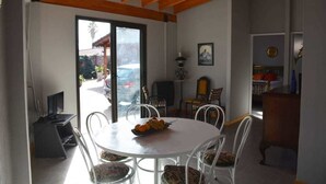A dining area with a round table and chairs, a laptop on a stand, and a window with a view of a parked car and greenery outside. - El Fresno (Mendoza)