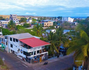 A multi-story building with a red roof, located in a residential area with visible palm trees and other houses. - The Island Home (Puerto Ayora)