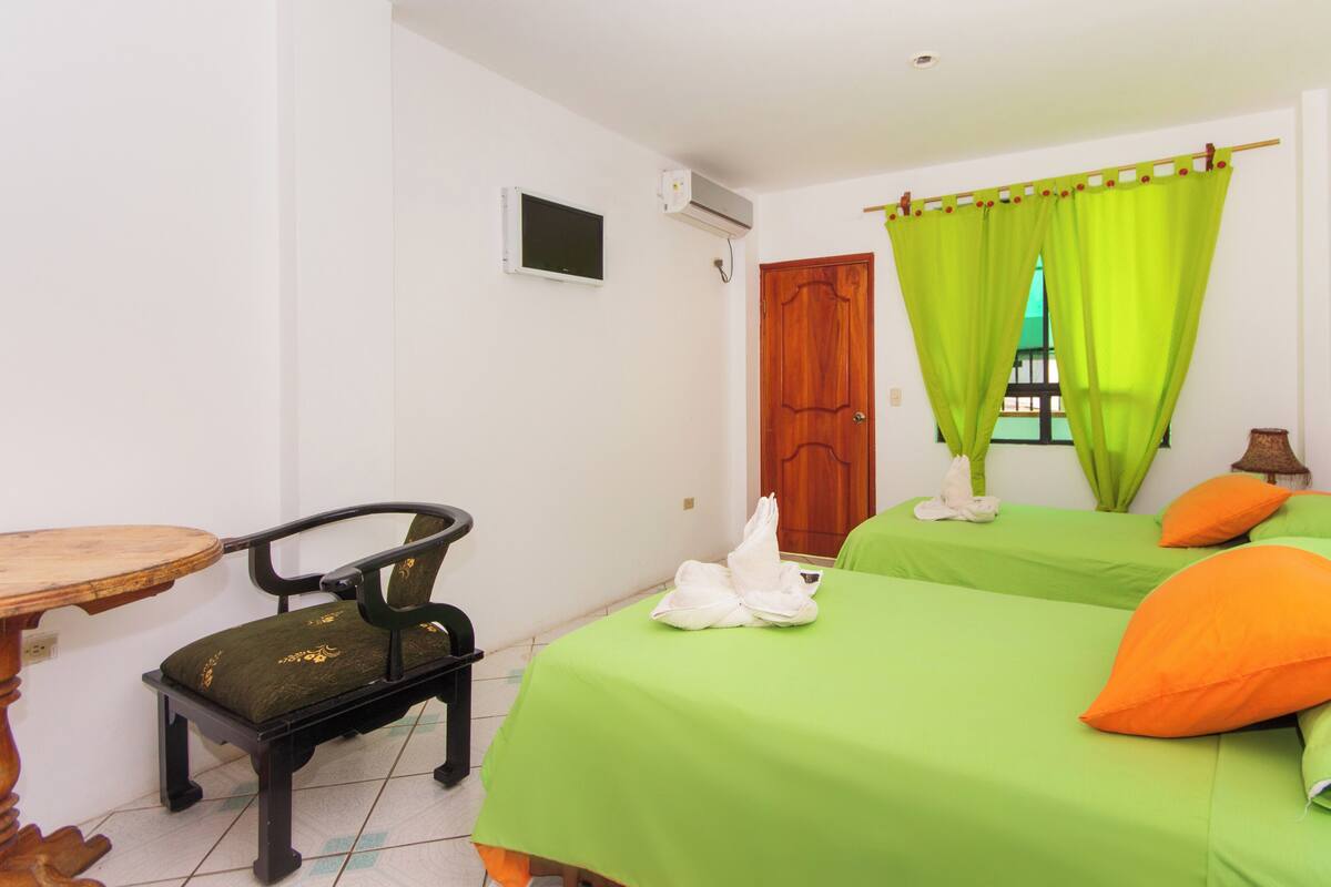 A room with two beds, a chair, a table, and a window with curtains.