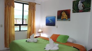 A hotel room with two beds, a window with curtains, a lamp, and wall art. - The Island Home (Puerto Ayora)