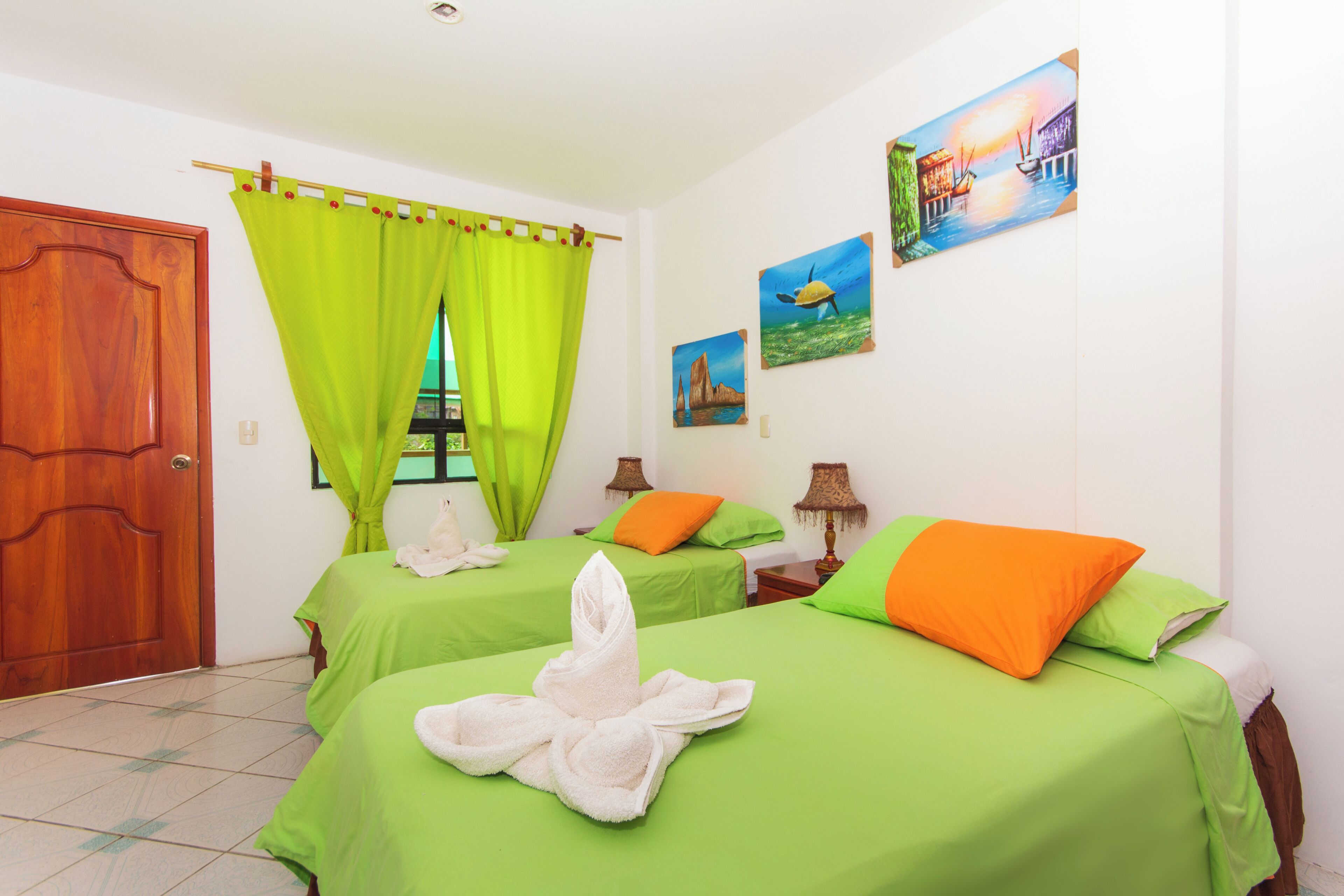 A hotel room with two beds, green bedding, a wooden door, and a green curtain.