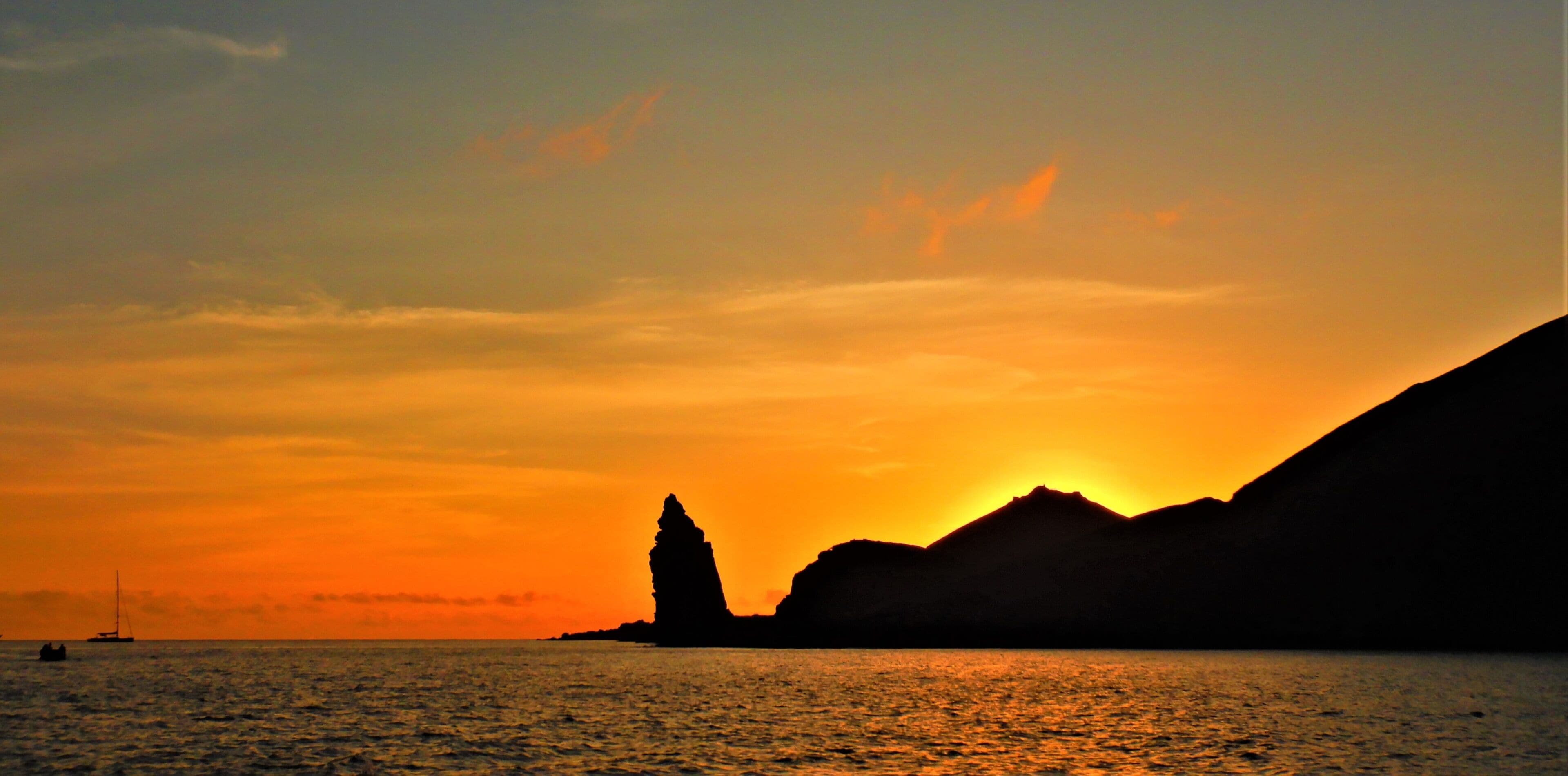 A sunset over water with a silhouette of a mountain and a rock formation.