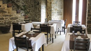 Un restaurant aux murs de pierre, nappes blanches et chaises en bois.