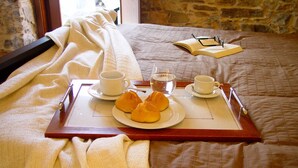 Un plateau avec une tasse, une soucoupe, une théière et des pâtisseries, posé sur un lit recouvert d’une couverture matelassée, avec un livre en arrière-plan.