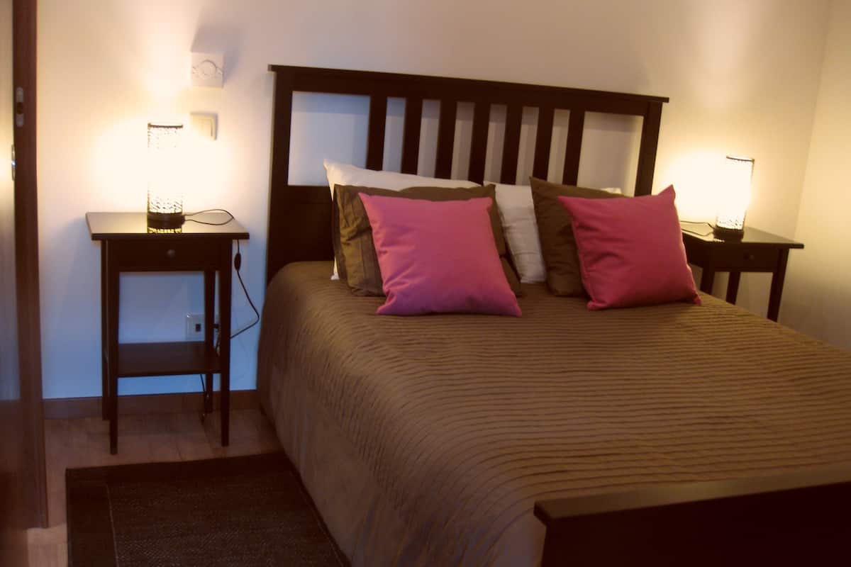 Una cama bien tendida con un cabecero de madera, flanqueada por dos mesitas de noche con lámparas.