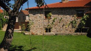 Une maison en pierre avec un toit recouvert de tuiles rouges, une balançoire et une pelouse bien entretenue.