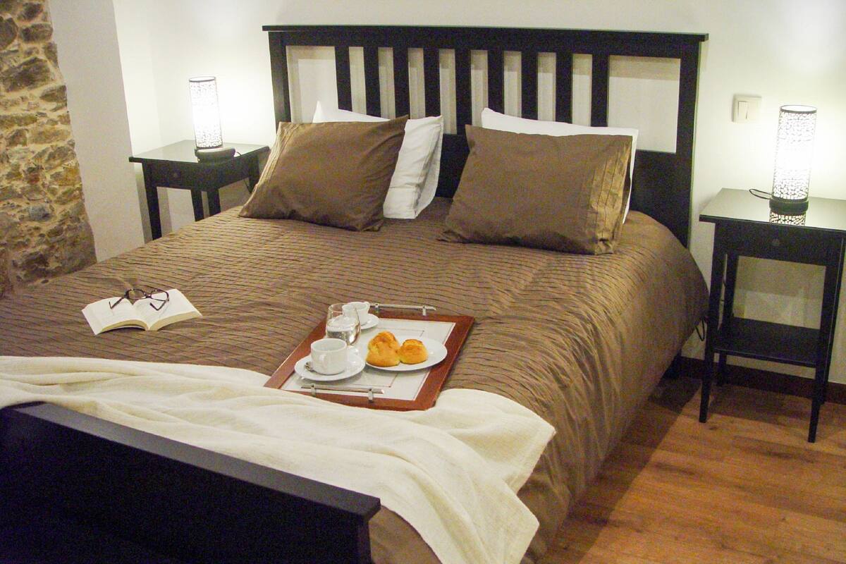 Una cama bien hecha con una bandeja de desayuno, un libro y un par de gafas sobre la misma.