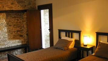 A room with two single beds, wooden headboards, a stone wall, and a window with a door.