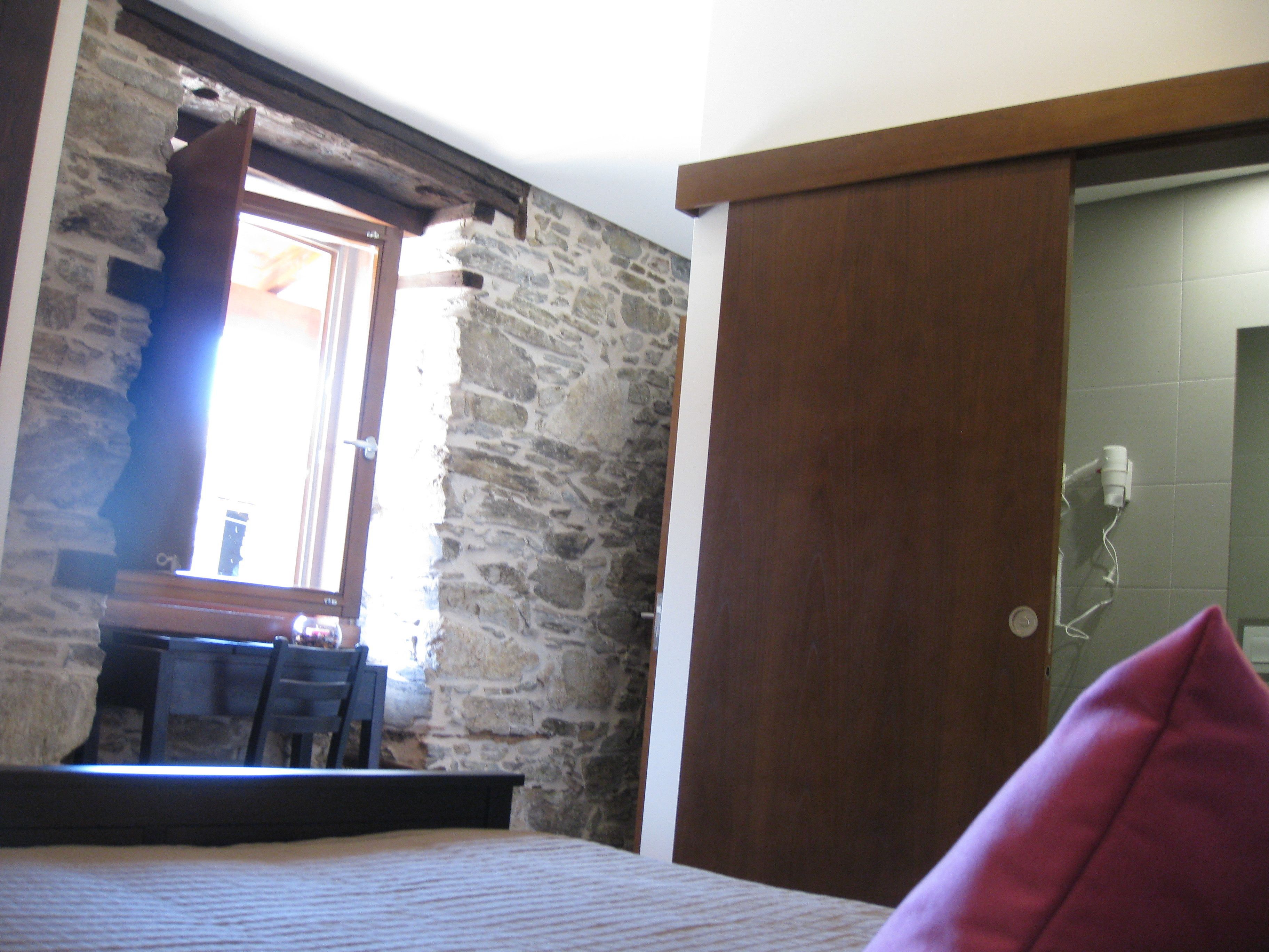 Un dormitorio con pared de piedra, puerta de madera y ventana.