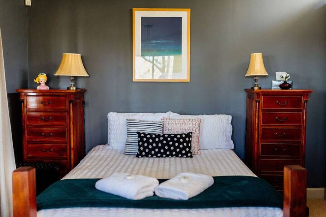 A neatly made bed with pillows and a blanket, flanked by two wooden nightstands with lamps and decorative items.