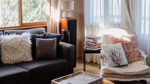 A living room with a dark sofa, a white armchair, a lamp, and a window with curtains. - Black Cockatoo - Secret Garden Mountains Home (Katoomba)