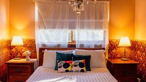 A bedroom with a bed, two bedside tables, a chandelier, and a window with a sheer curtain. - Black Cockatoo - Secret Garden Mountains Home (Katoomba)