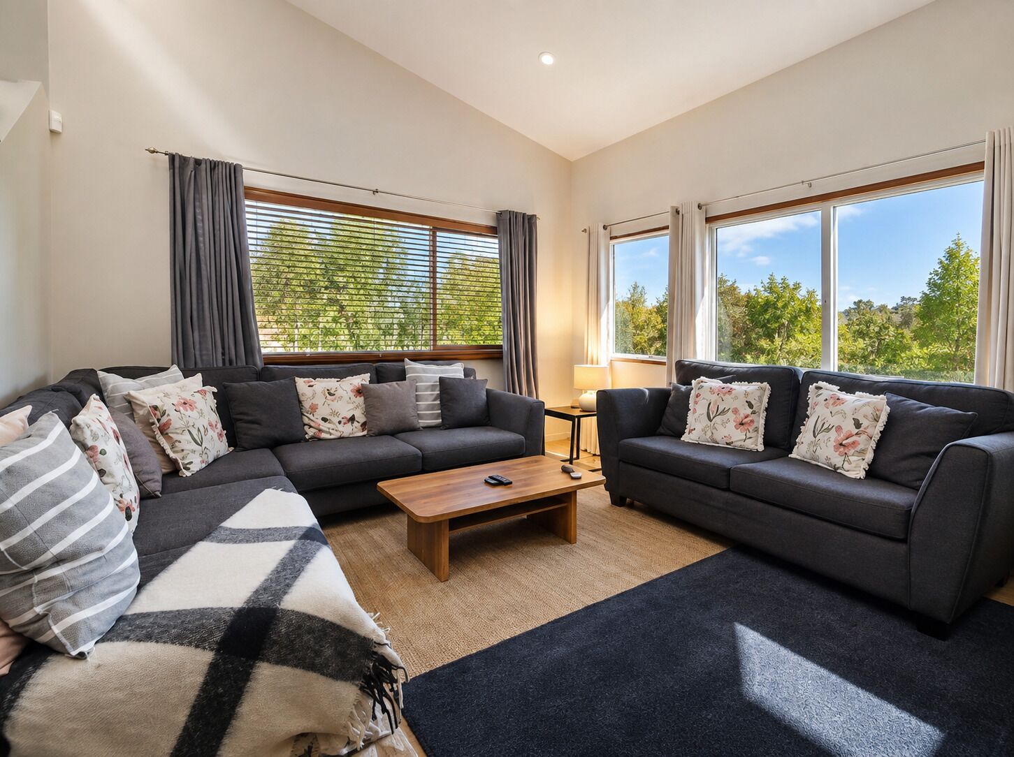 A modern living room with two sofas, a coffee table, and a view of greenery through large windows.
