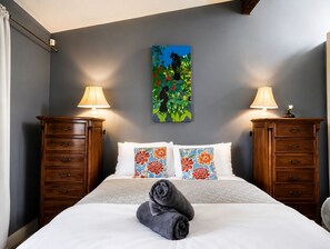 Una habitación de hotel con una cama, dos mesitas de noche, un cuadro y una ventana con cortinas.